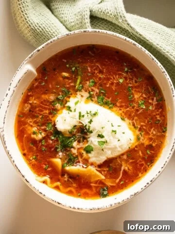 Lasagna soup in a bowl with a dollop of ricotta garnished with parsley and parmesan.