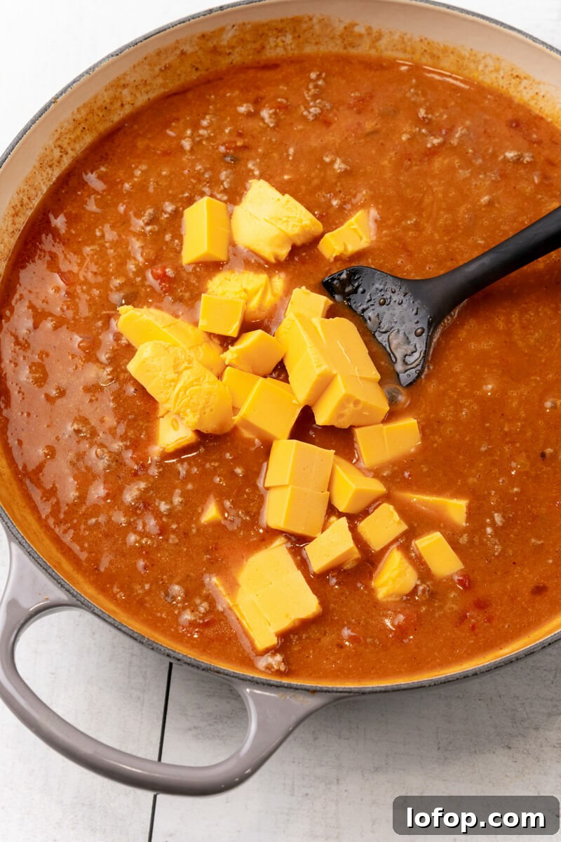 Chunks of Velveeta cheese are added to the sauce and stirred in.