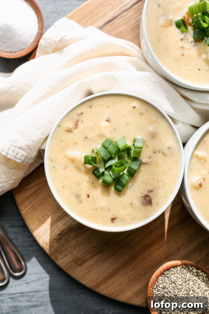three white bowls of gluten free instant pot baked potato soup with green onions on top sitting on a round, wooden cutting board