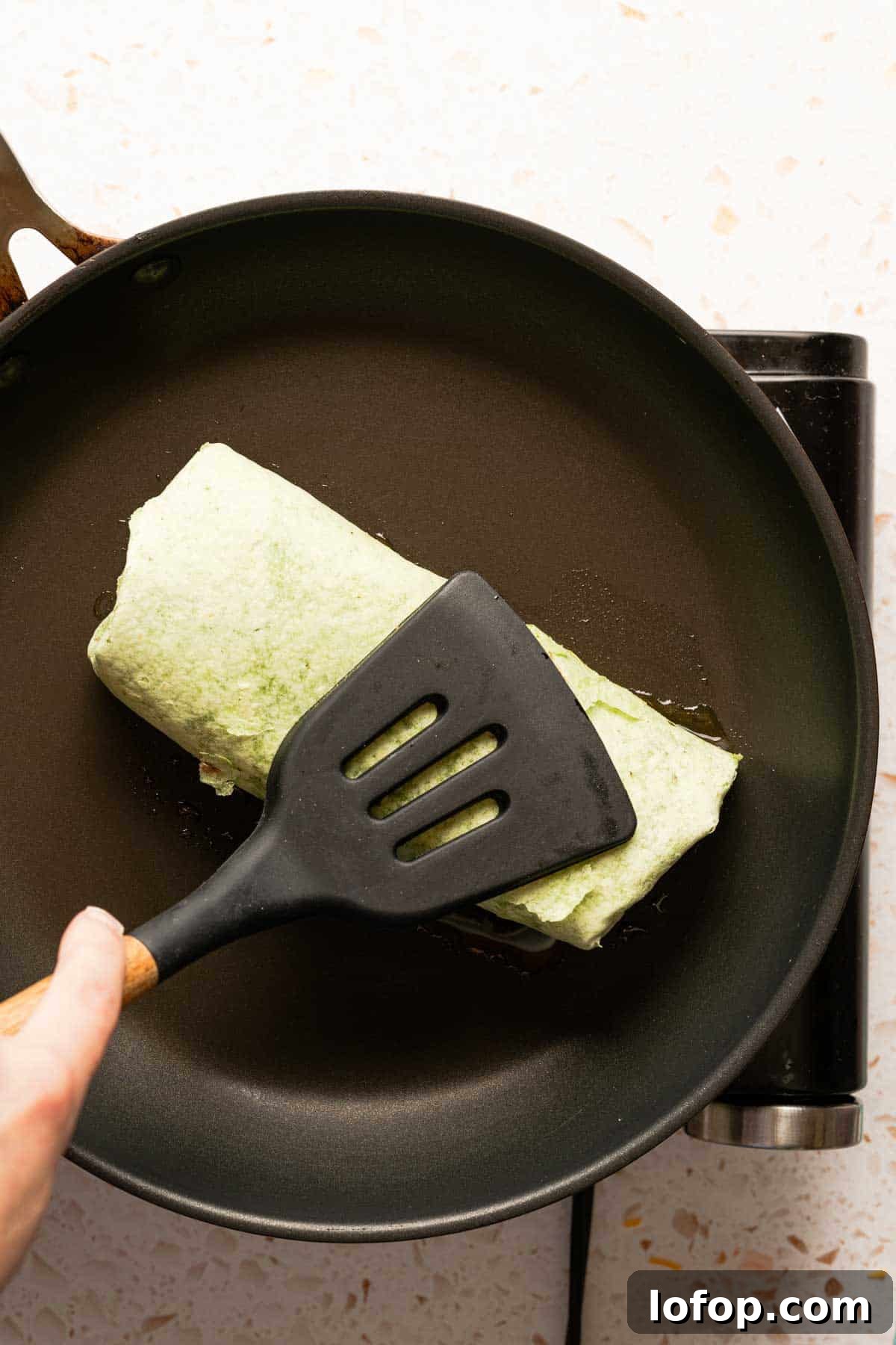 Crispy Tuna Melt Wrap Recipe for Quick Lunches 13 tuna melt wrap being pressed down in pan with spatula.