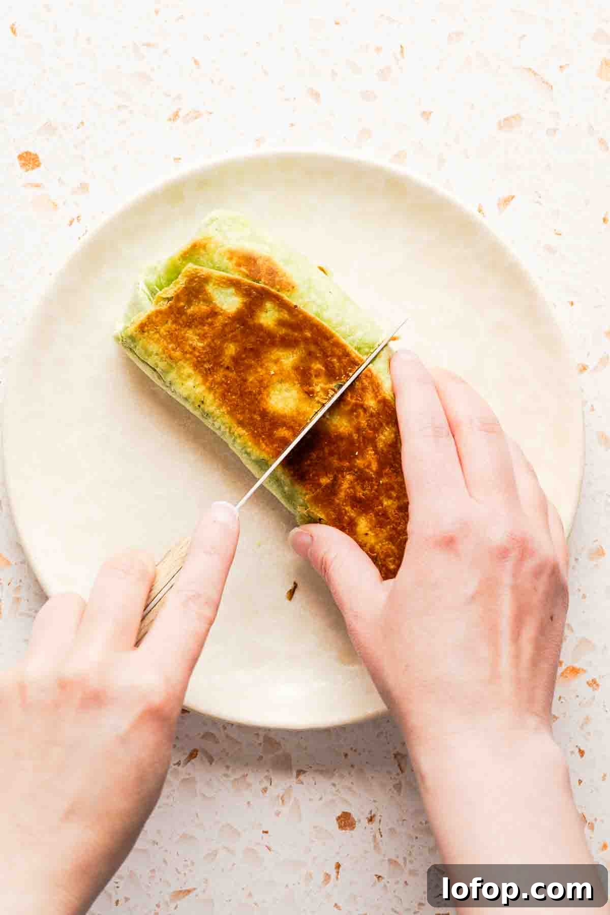 Crispy Tuna Melt Wrap Recipe for Quick Lunches 16 wrap sandwich being cut in half on white plate.