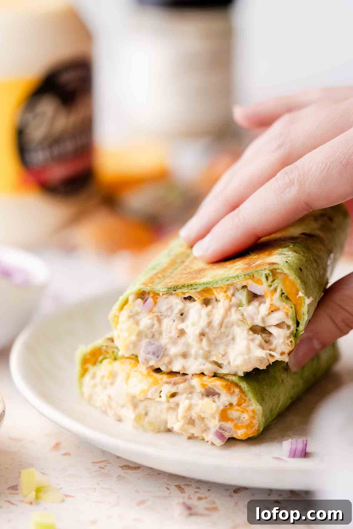 Crispy Tuna Melt Wrap Recipe for Quick Lunches 17 hand picking up half of tuna melt wrap stacked on plate.