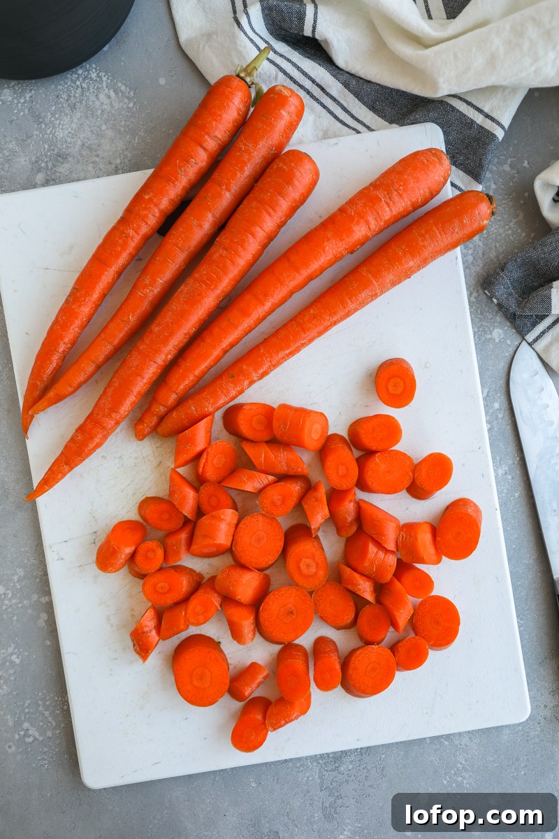 Large whole carrots sitting on a white cutting board next to freshly cut carrot slices