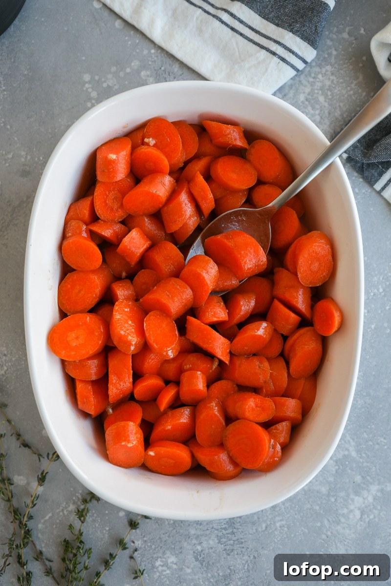 Fresh carrots cut on the bias in a large white owl tossed in a garlic and brown butter maple sauce ready for the oven