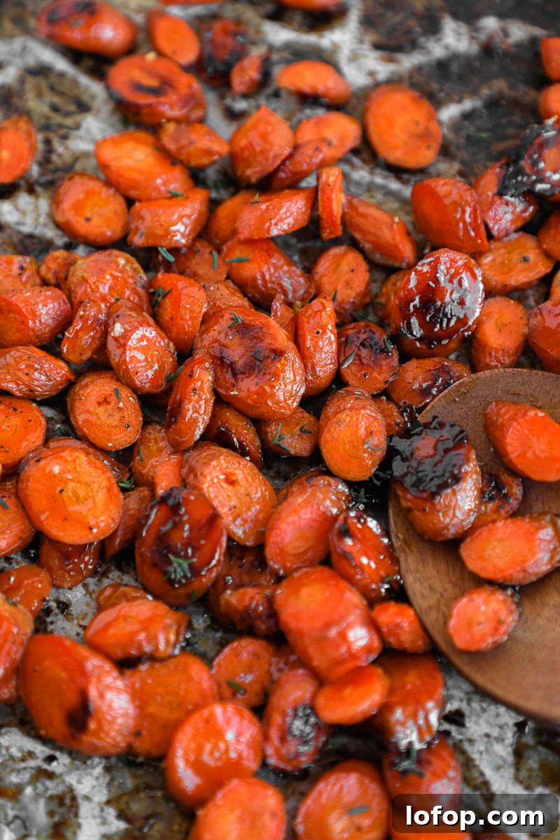 Crispy roasted carrots slices drizzled in a sweet maple glaze on a metal sheet pan with a wooden spatula
