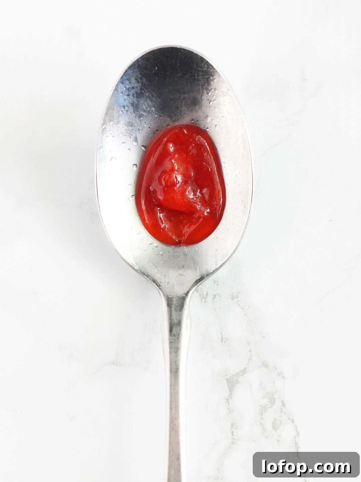 Drop of strawberry preserves in the middle of a cold metal spoon.