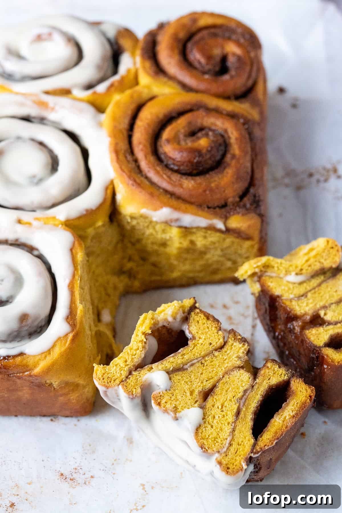 Vegan pumpkin cinnamon rolls on a piece of white baking parchment, one sliced in half.
