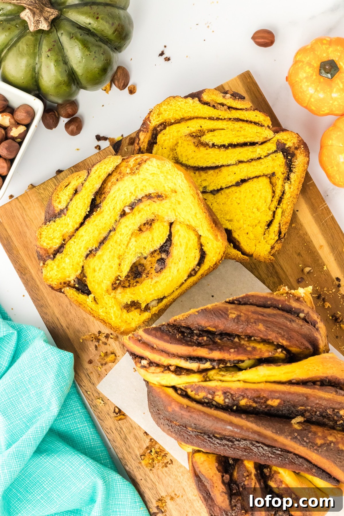Top down view of a loaf of twisted chocolate pumpkin bread dotted with crushed hazelnuts. The front of the loaf is slices showing a top down view of the swirls. Hostess At Heart
