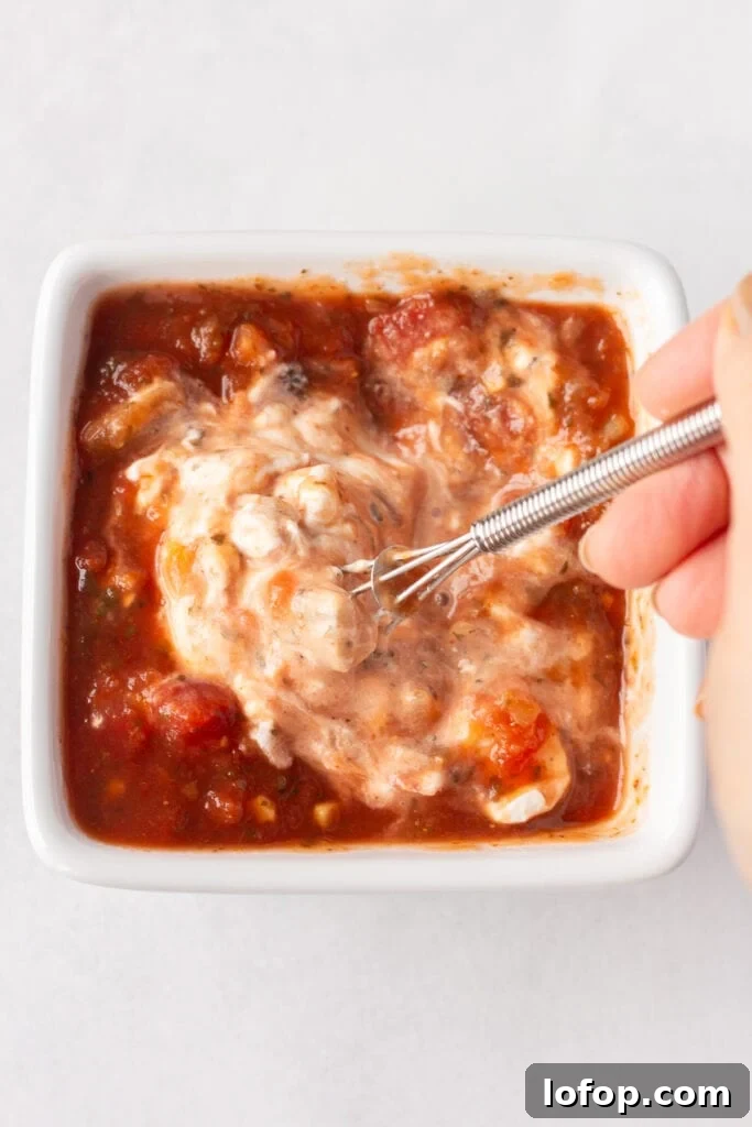 Sour cream and salsa being mixed together with a whisk in a white square dish.