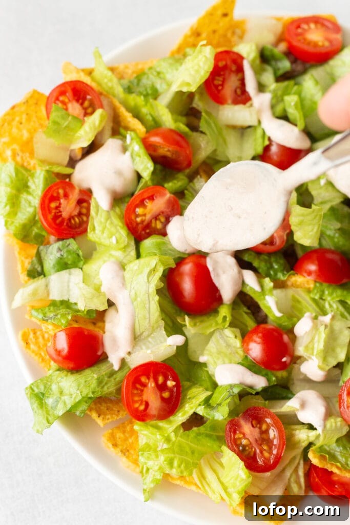 A spoon dripping salsa sour cream dressing onto a plate of nacho salad.