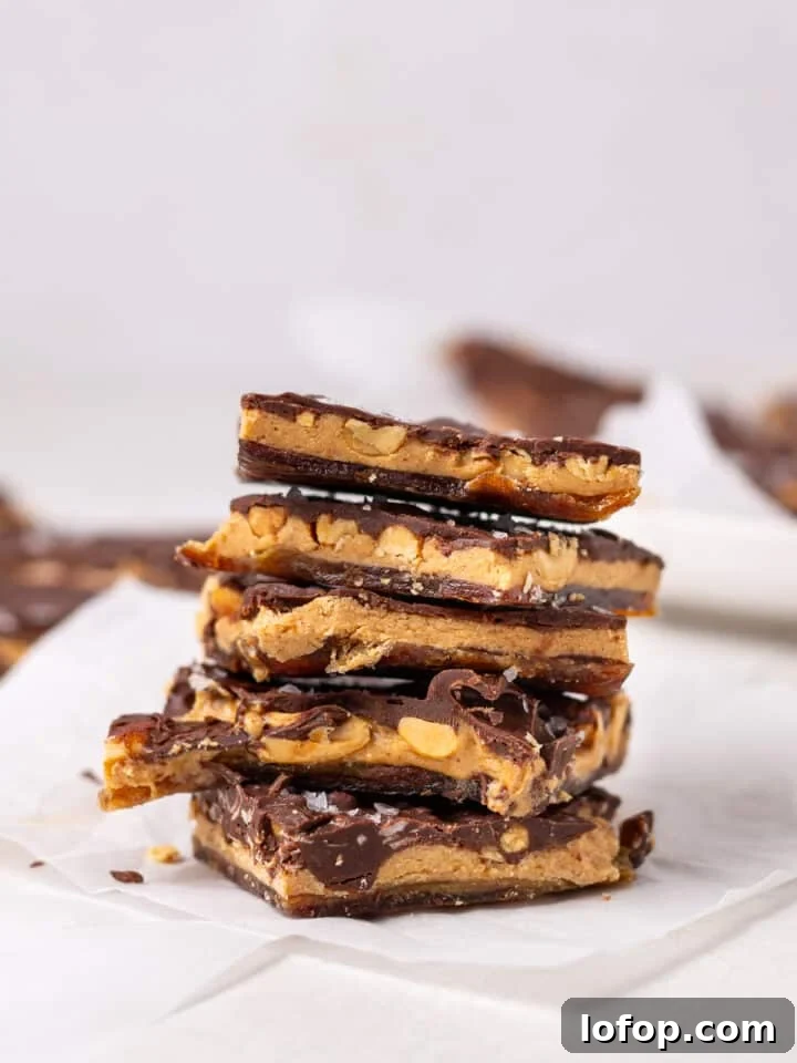 Stacked pieces of date bark with chocolate, peanut butter, chopped peanuts, and flaky sea salt on parchment paper
