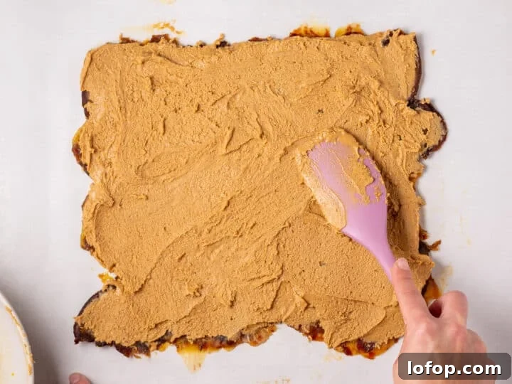 Peanut butter mixture being spread over the flattened date layer with a pink spatula