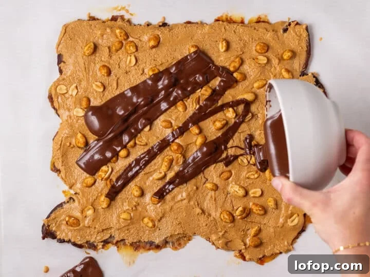 Melted chocolate being poured over the peanut butter and peanut layer