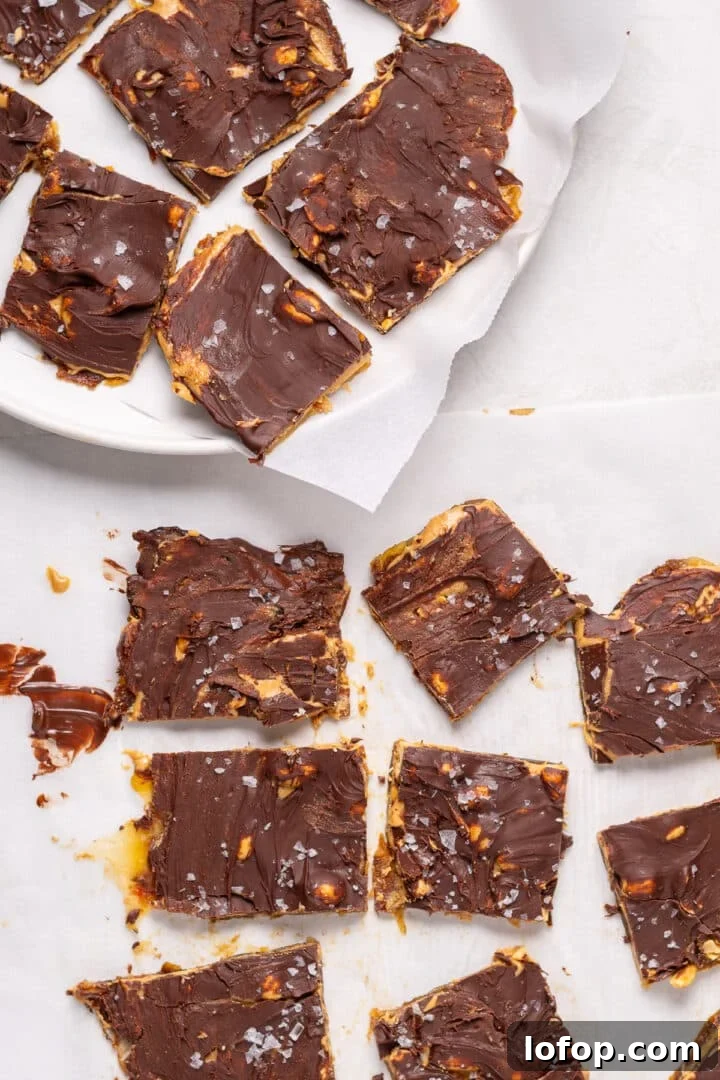 Sliced pieces of snickers date bark topped with melted chocolate, peanuts, and flaky sea salt on parchment paper