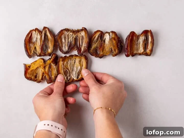 Hands pressing opened dates flat on a sheet of parchment paper
