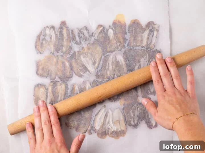 A rolling pin flattening dates between two sheets of parchment paper