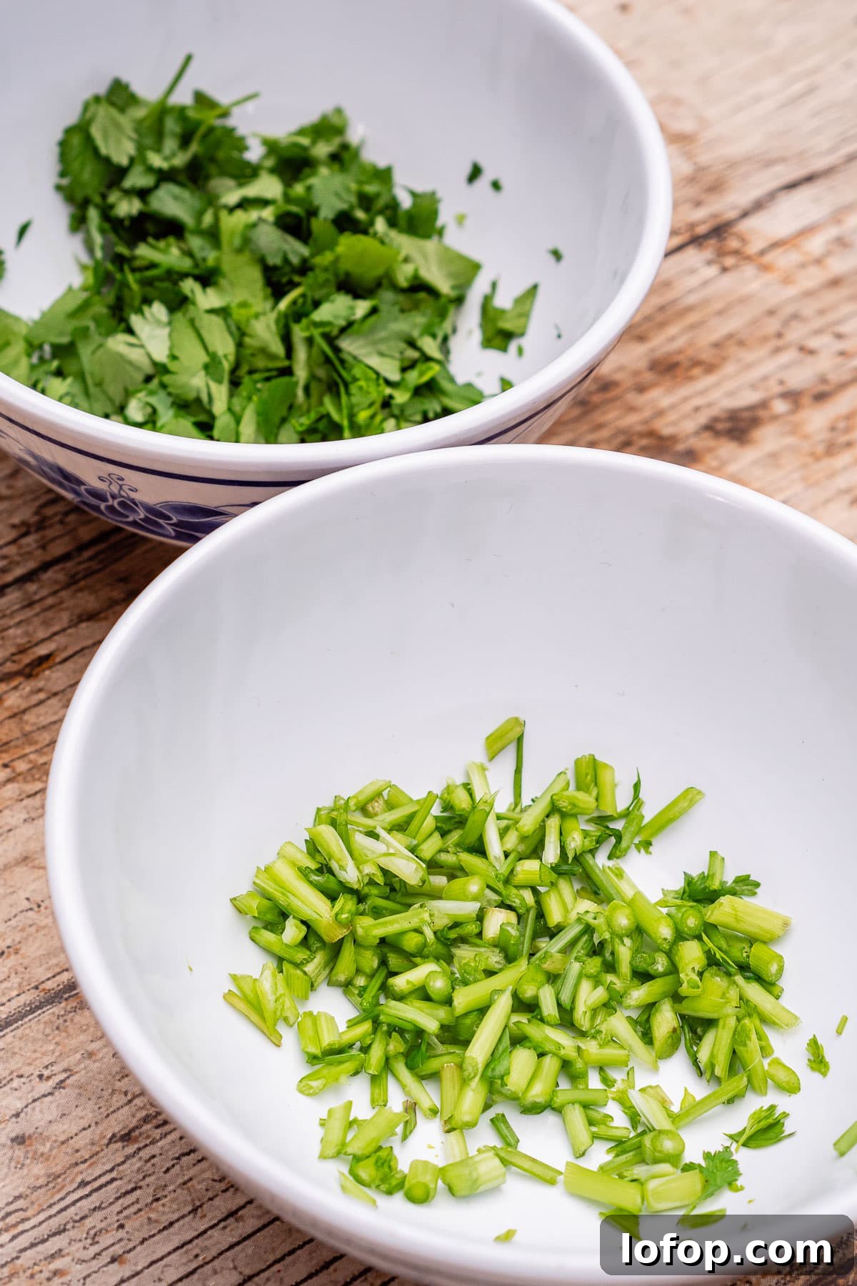 Chopped coriander stems in a white bowl and chopped coriander leaves in another bowl
