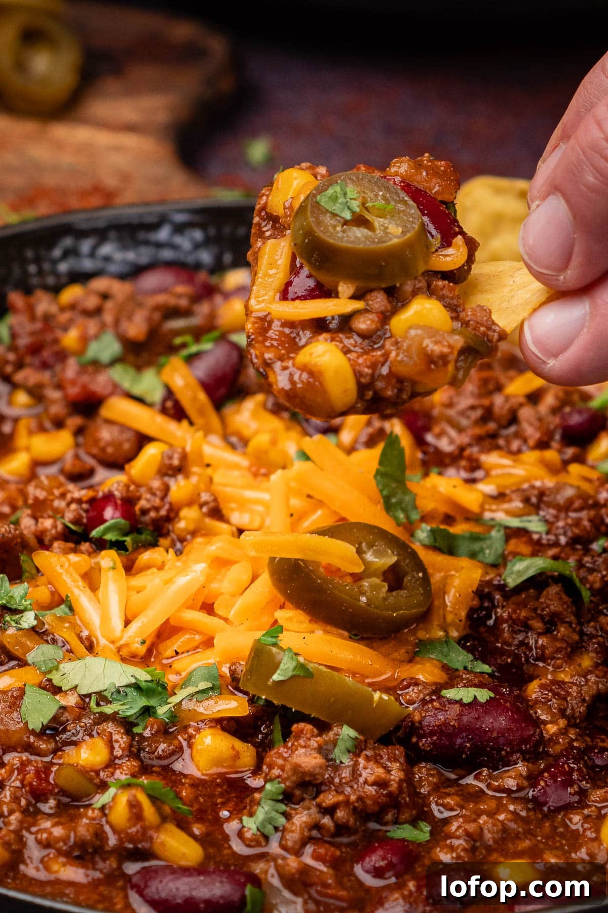 Dipping a tortilla chip by hand in chilli con carne with a jalapeno on top
