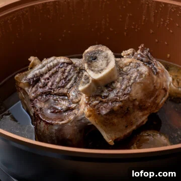 A cooked beef shin in a slow cooker on a vegetable trivet and gravy