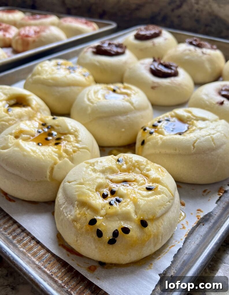 Freshly baked sourdough kolaches with jam centers cooling on a parchment-lined baking sheet.