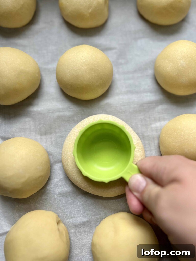 Pressing indentations into sourdough kolache dough rounds with the bottom of a measuring cup before adding filling.