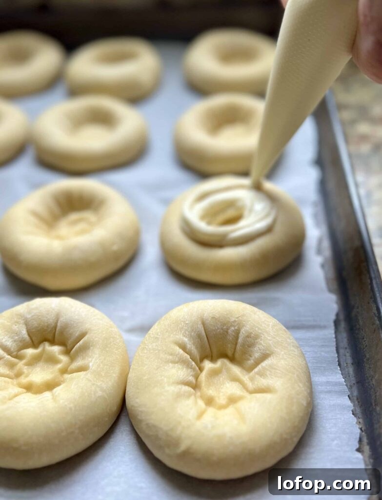 Piping cream cheese filling into sourdough kolache dough rounds.