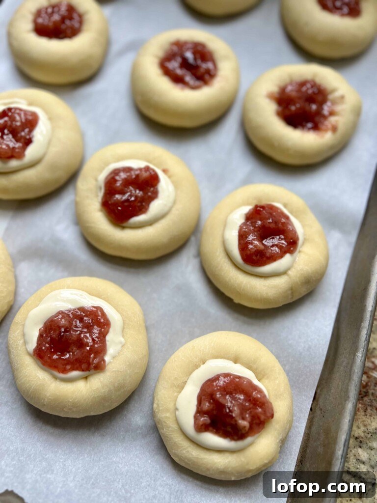 Sourdough kolaches filled with fruit jam and cream cheese filling on a baking sheet before baking.