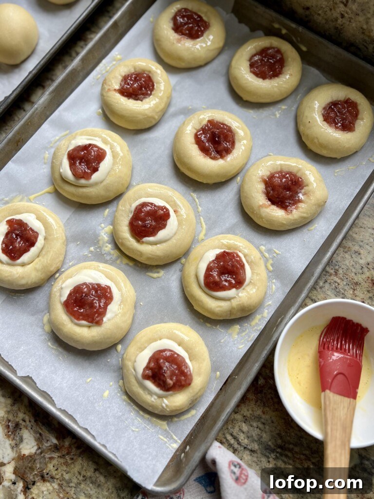 Tray of unbaked sourdough kolaches with cream cheese and fruit jam filling ready for the oven.