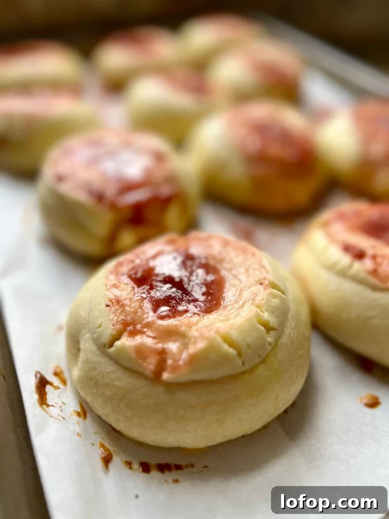 Freshly baked sourdough kolaches with fruit jam centers cooling on a parchment-lined baking sheet.