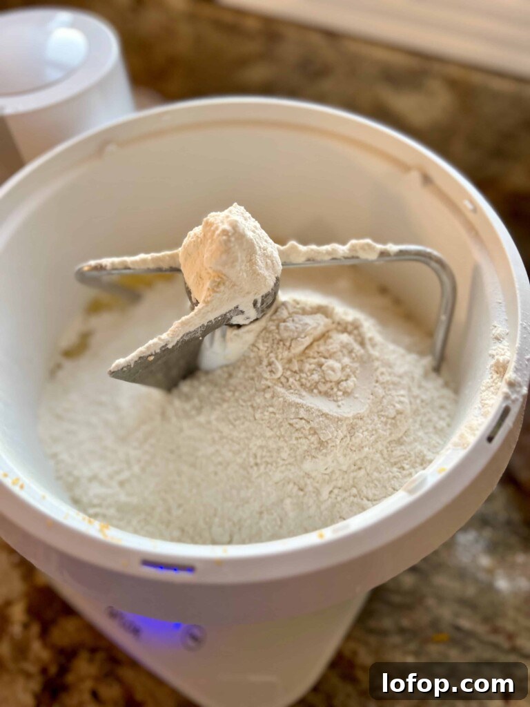 Flour and ingredients for sourdough kolache dough sitting in the bowl of a mixer.