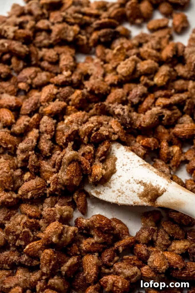 Cinnamon Sugar Candied Almonds Recipe | Crunchy Roasted Almonds 8 Someone is using a spatula to spread candied almonds onto a baking sheet.