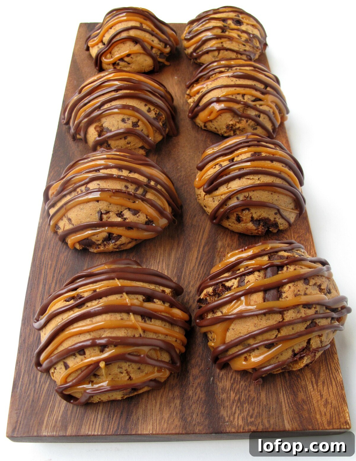 Wooden cutting board with two rows of rounded cookies decorated with chocolate and caramel zigzags.