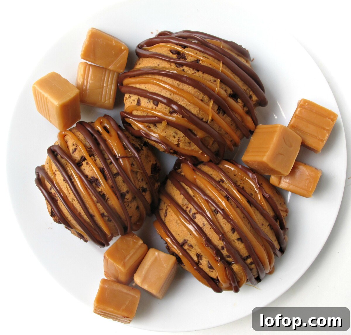 Overhead three cookies on a white plate with candy caramel squares.