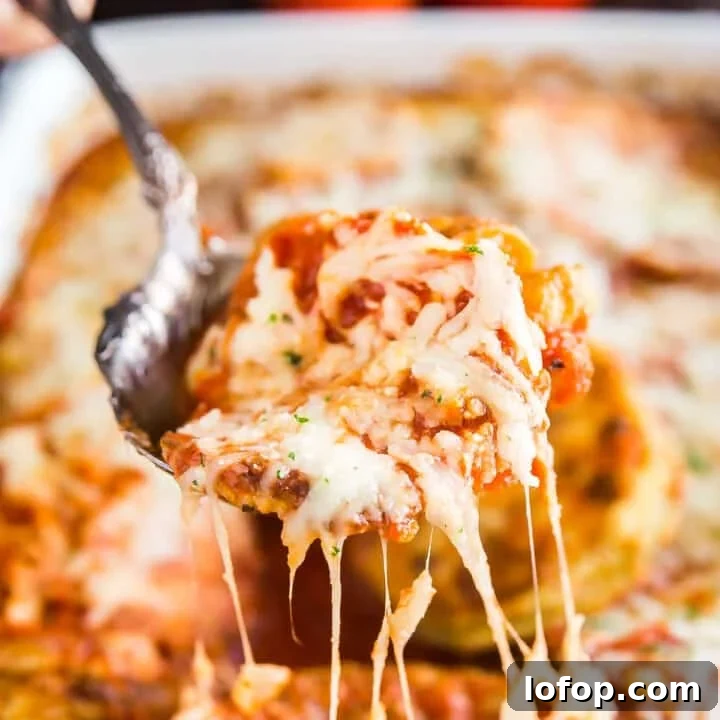 A spoon lifting up a scoop of eggplant parm bake with melt cheese trailing behind it.