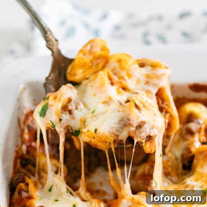 A spoon pulling a scoop of baked tortellini from the pan with melted cheese stretching.
