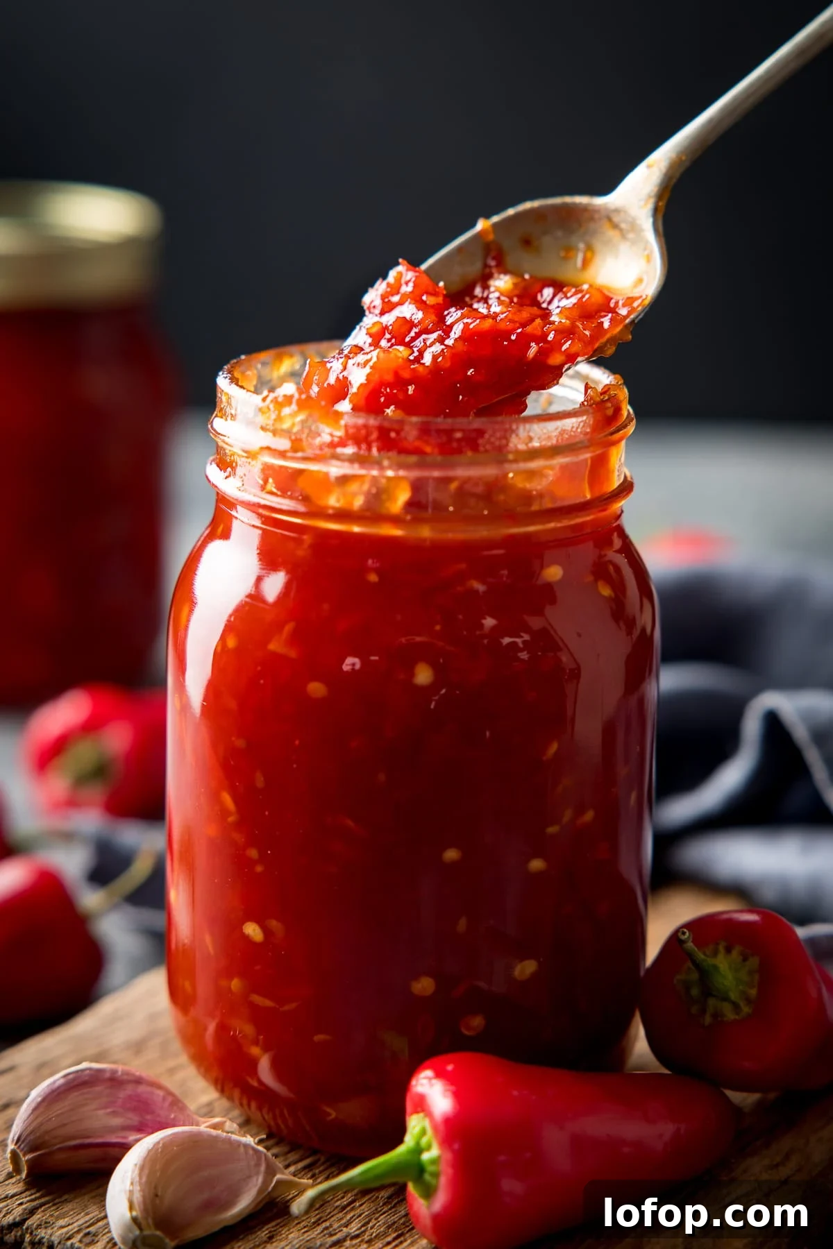 Spoonful being taken from a jar of sweet chilli sauce. Ingredients scattered around the jar.