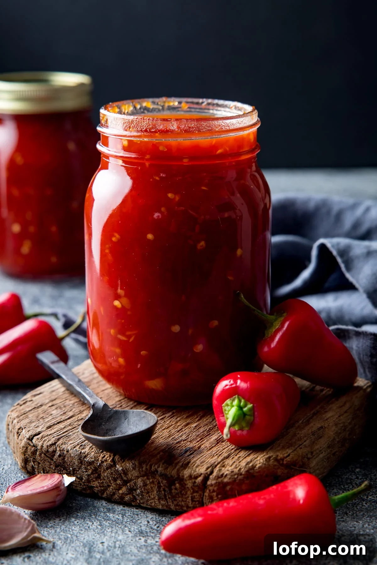 Jar of sweet chilli sauce with a board next to a spoon and some fresh chillies