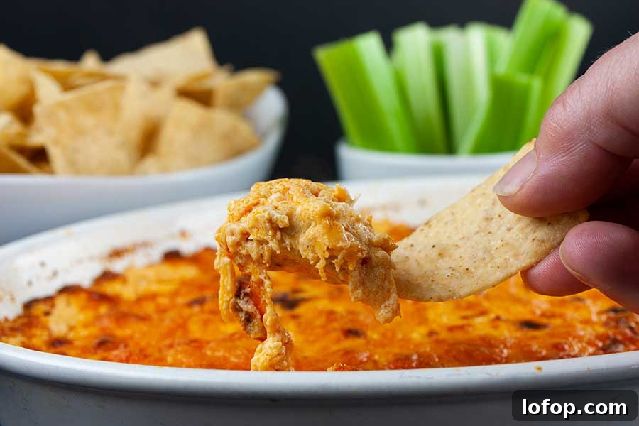 Creamy Buffalo Chicken Dip Recipe for Game Day and Parties 2 Buffalo chicken dip lifted out of the baking dish with a tortilla chip.