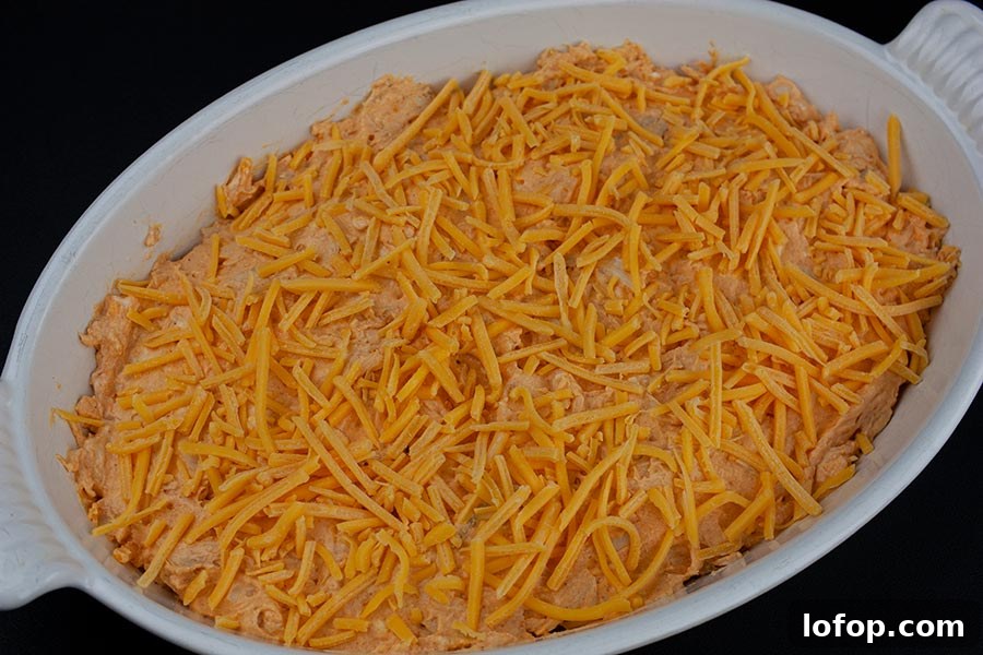 Creamy Buffalo Chicken Dip Recipe for Game Day and Parties 5 Buffalo Chicken Dip - unbaked dip in a white casserole dish topped with cheddar cheese