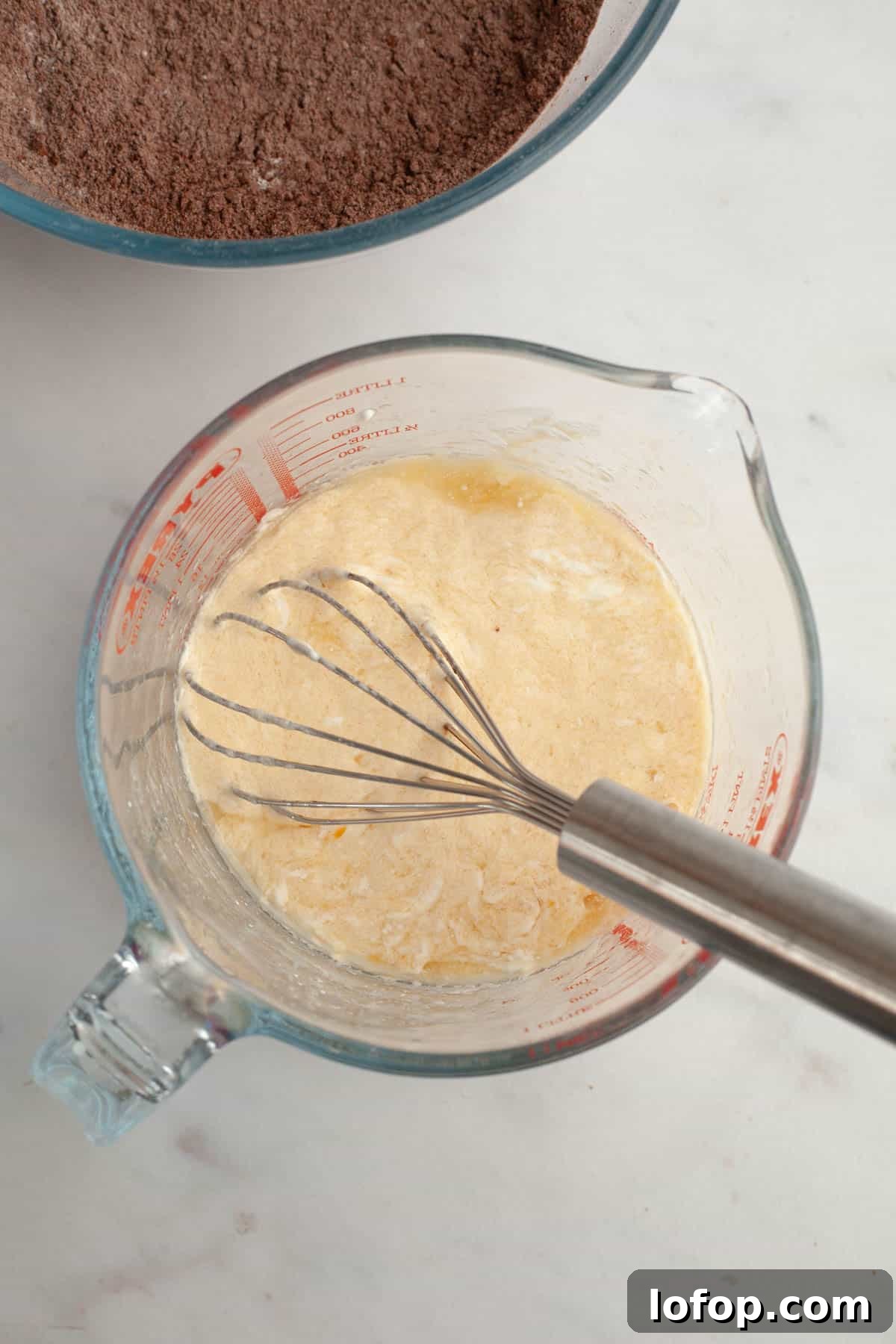 Decadent Chocolate Cupcakes with Cream Cheese Frosting 5 A glass jug with a silver whisk and a light yellow mixture in it.