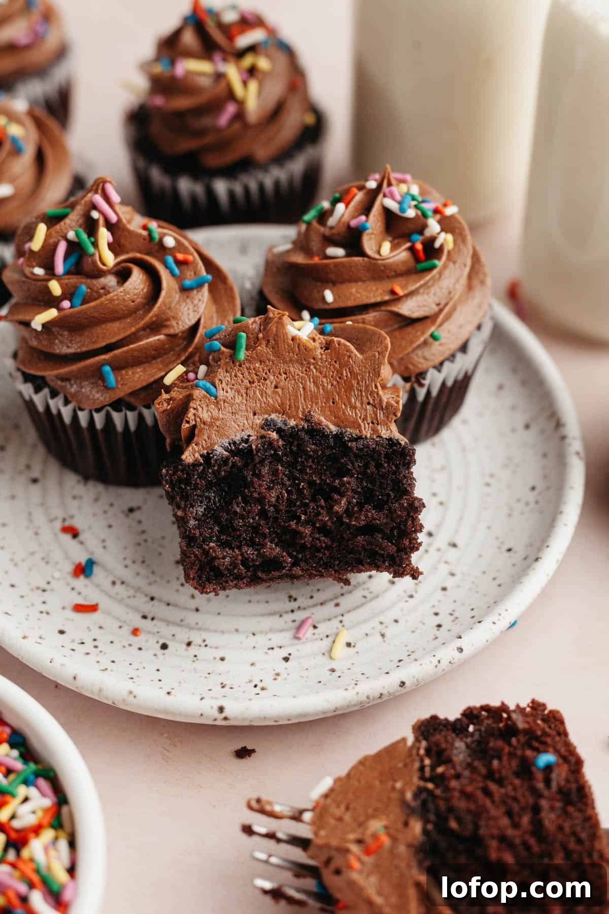 Decadent Chocolate Cupcakes with Cream Cheese Frosting 10 Three chocolate cupcakes on a plate, one has been cut in half.