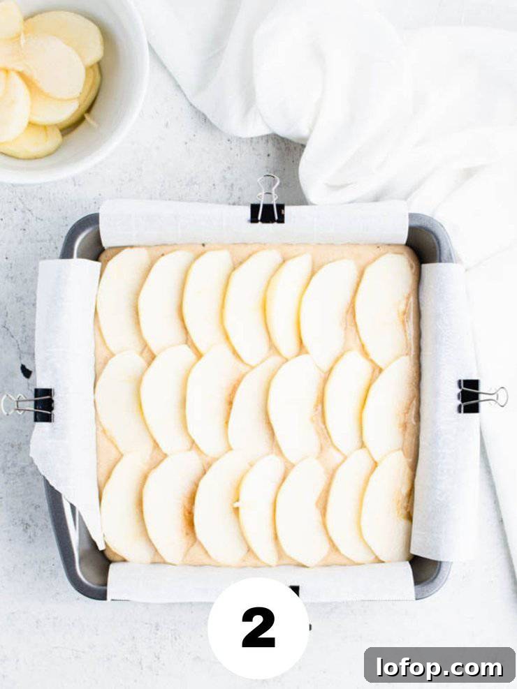 cake batter in a square pan covered with sliced apples.