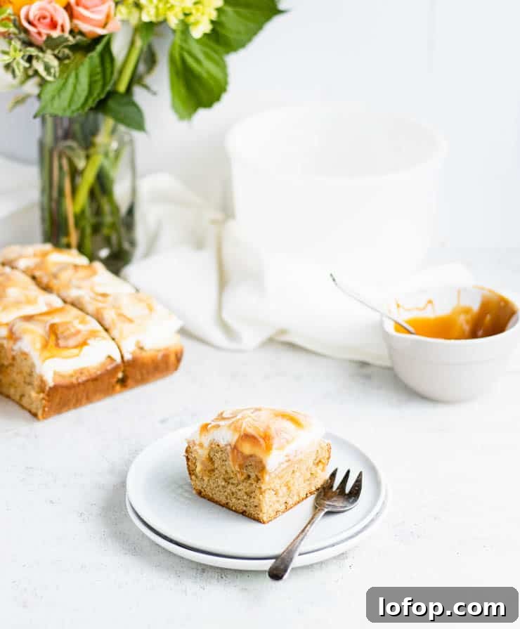 square slice of caramel apple cake on a blue plate with a bouquet of yellow and white flower and the rest of the cake in the background.