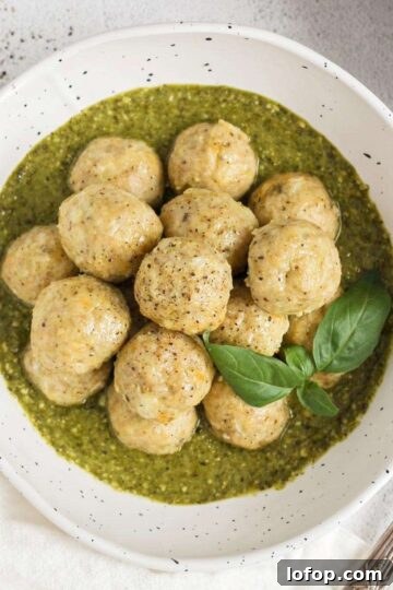 Chicken meatballs stacked in a bowl with pesto with a small bowl of pesto on the side.
