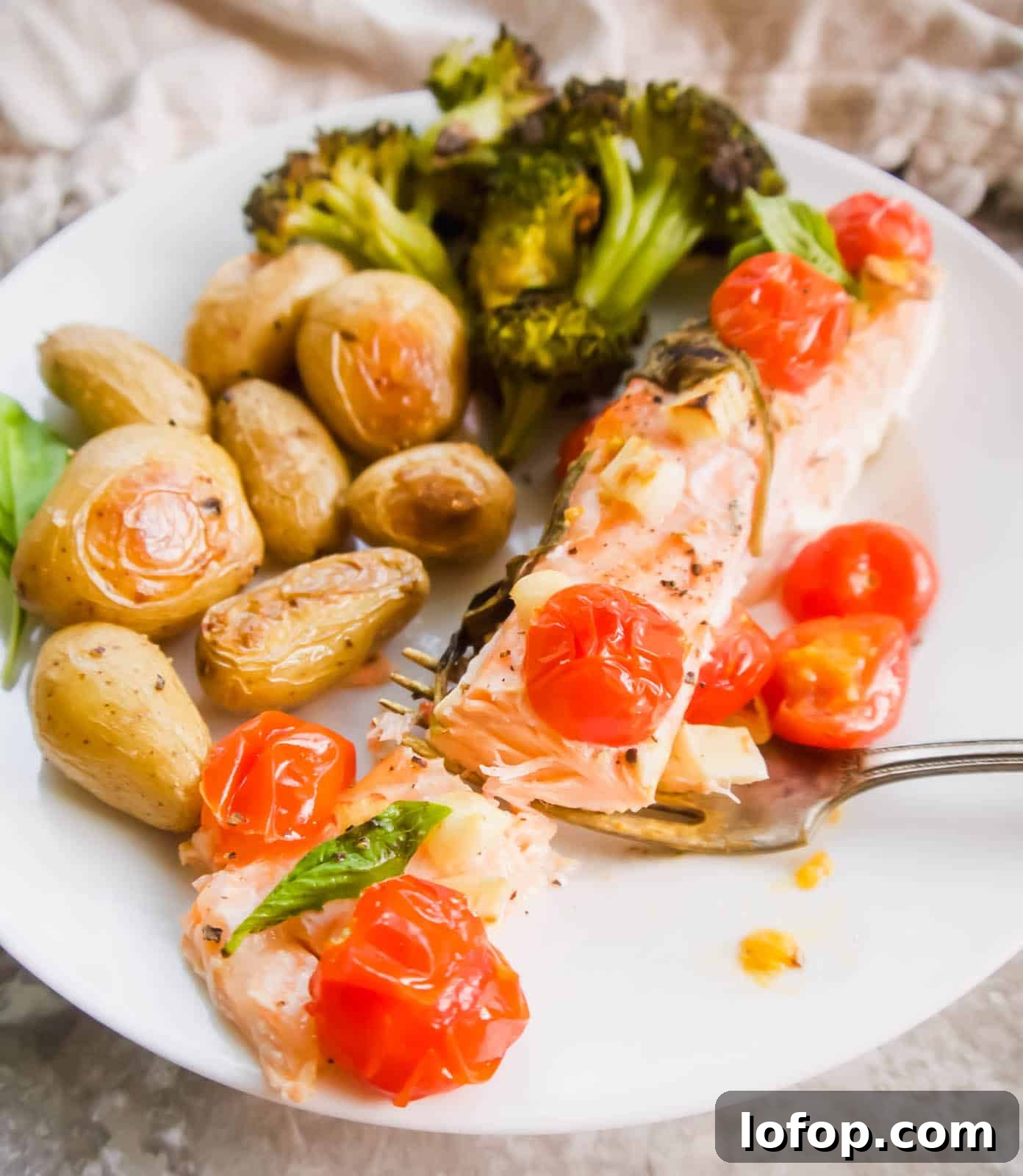 Baked salmon with tomatoes on a plate with potatoes and broccoli.