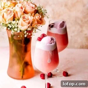 Two glasses of rosé sorbet floats garnished with raspberries next to a vase with Mother's Day flowers.