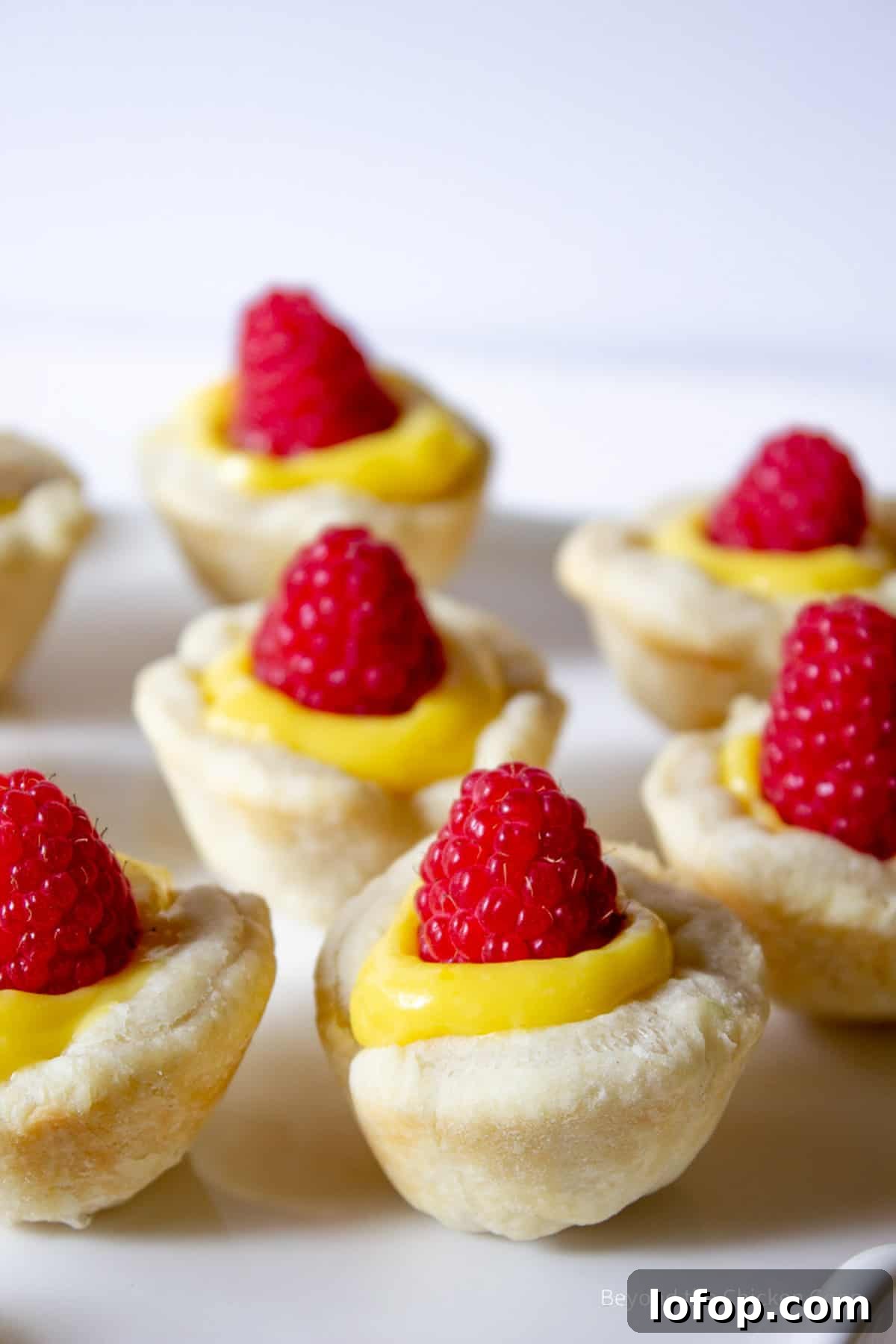 Mini Lemon Tarts Recipe: Zesty Bite-Sized Citrus Pastries 10 Mini Tarts topped with a fresh raspberry.