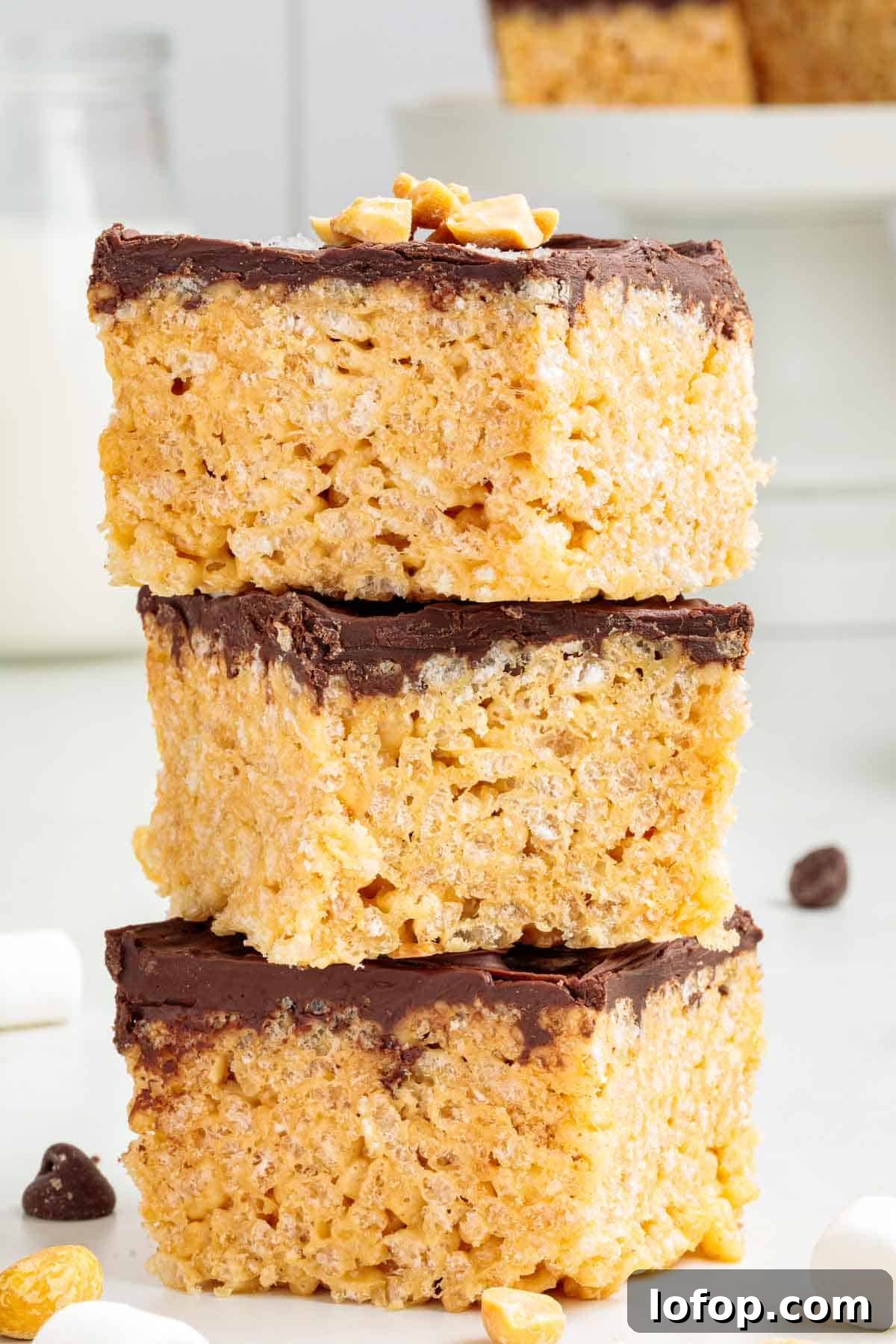 Chocolate Peanut Butter Rice Krispie Treat Recipe 13 A stack of three thick chocolate-covered Rice Krispie treats with visible crispy cereal texture and chopped peanuts on top.