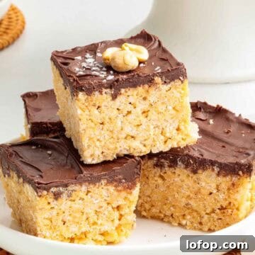 Chocolate Peanut Butter Rice Krispie Treat Recipe 14 A stack of four chocolate peanut butter Rice Krispie treats on a plate, each with a glossy chocolate top and lightly salted chopped peanuts for garnish.