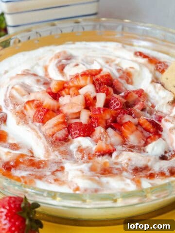 Strawberry cheesecake dip topped with swirled strawberry jam and diced fresh strawberries served in a glass pie dish.